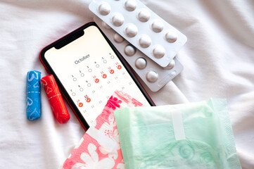 Smartphone displaying a menstrual calendar with sanitary pads, tampons, and blister packs of pills...