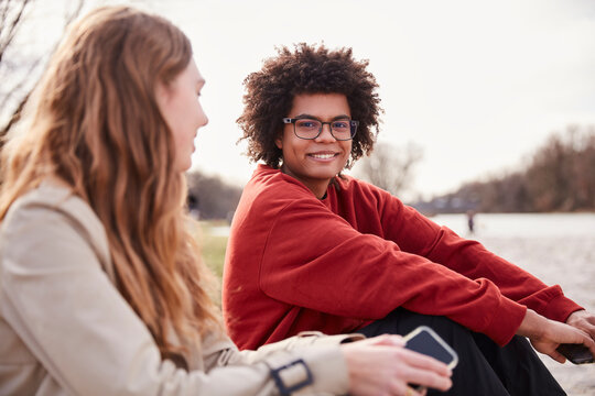 Young mixed race guy and European girl sitting outside along a river hanging out. Munich, Germany