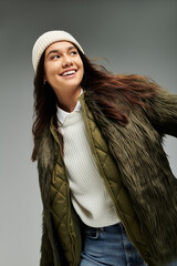 A young woman wearing a chic fur jacket and beanie radiates happiness in a minimalist setting.