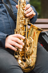 A saxophonist performs in a serene park during autumn while seated on a bench surrounded by fallen...