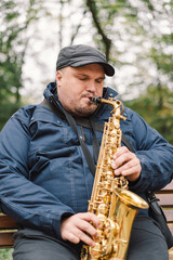 A saxophonist performs in a serene park during autumn while seated on a bench surrounded by fallen...