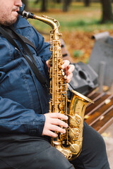 A saxophonist performs in a serene park during autumn while seated on a bench surrounded by fallen...