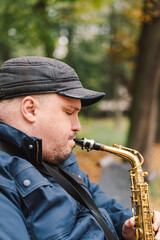 A saxophonist performs in a serene park during autumn while seated on a bench surrounded by fallen...