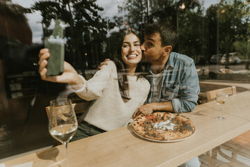 A joyful couple enjoys a cozy meal together at a rustic café, savoring pizza and drinks on a sunny afternoon