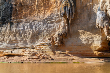 Limestone cliffs with unique erosion patterns and lush vegetation. Canoe ride along the yellow river water. Manambolo River, Madagascar.