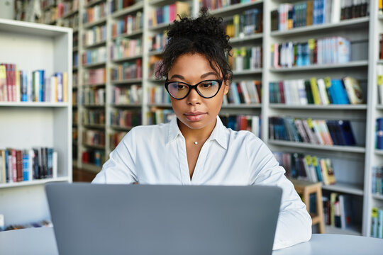 A dedicated teacher reviews materials on her laptop while surrounded by shelves filled with books.
