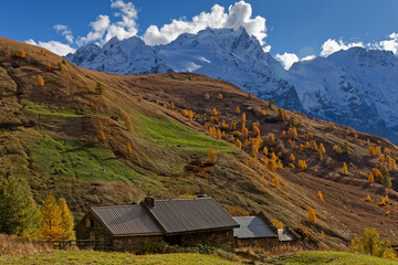 A hut under orange forest, green pastures and white peaks in La Meije massif