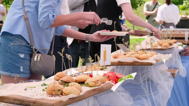 Guests help themselves to plates at an elegant open buffet. Attendees enjoy a variety of sandwiches under sunny skies. Perfect for events and lifestyle themes