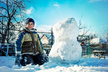 boy sculpt a snowman in the backyard of the house clear winter day. The boy rolls a snowball to build a snowman in the yard during a heavy snowfall. toned.
