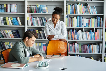 A teacher attentively supports her student in a vibrant library filled with books.