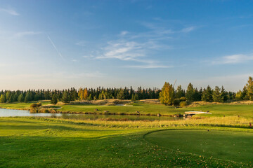 A landscape of golf courses with green grass, a natural pond, against a blue sky.