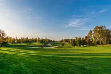 Magnificent view of the golf course with bright green grass and ponds on a clear autumn day.