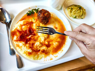 A person enjoys a delicious meal featuring creamy mashed potatoes and meatball with sauce at a dining table