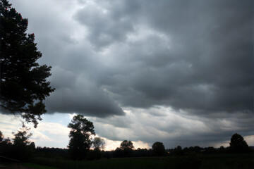 Obraz premium Thick grey clouds dominate the sky, hinting at an approaching storm near the serene countryside landscape