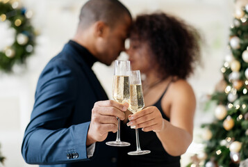 Cheers. African american couple clinking champagne glasses celebrating Christmas or New Year Eve together, toasting holidays, closeup. High quality photo