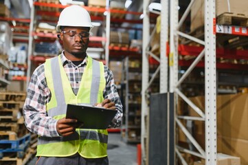 Portrait of african american warehouseman with clipboard checking delivery, stock in warehouse. Warehouse worker preparing products for shipment