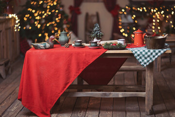 a beautiful setting of the New Year's table in red, against the background of a decorated Christmas tree. Christmas decorations. Christmas tree branches, teapot and cups on the table.