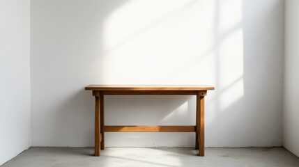 A simple wooden desk is next to a white wall. There is a lot of open space around it.