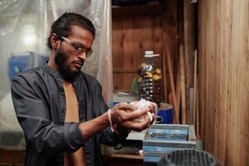 Male worker of plastic recycling workshop in protective eyeglasses looking at polyethylene bottle caps before processing them