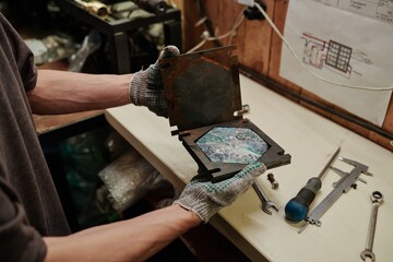Gloved hands of unrecognizable engineer of plastic recycling factory opening metal press mold with...