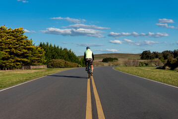 Male cyclist riding his bike in the middle of a road with a background of forests and mountains outdoors  