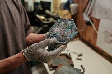 New reclaimed tile in gloved hands of unrecognizable engineer of plastic recycling factory standing by workbench