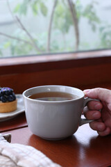 A cup of hot tea with black background, wood background, with a cup of hot tea in hand ,warm photo.