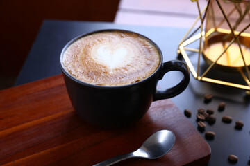 Side view of hot latte coffee with latte art in a bright black cup and saucer isolated on book dark background