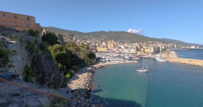 Scenic video over Bastia harbor wall and entrance with lighthouse under a bright blue sky