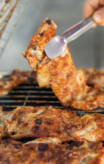 Traditional chicken grill over charcoal fire, one person checks if the chicken is cooked, selective focus.