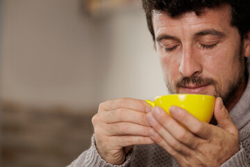 Man enjoying a cup of coffee on a break from work. Close-up of a handsome man, with a yellow cup of coffee in his hands. Moments of enjoying and relaxing.