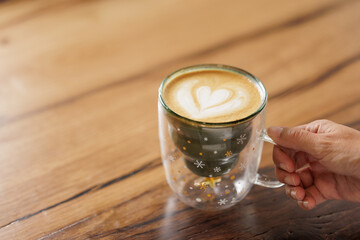 Hands of unrecognizable woman in red sweater sitting at table enjoying specialty coffee in cafe with Christmas mug with star drawings.