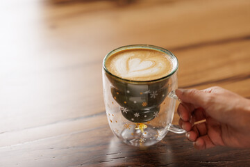 Hands of unrecognizable woman in red sweater sitting at table enjoying specialty coffee in cafe with Christmas mug with star drawings.