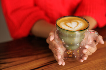 Young woman holding a cup with Christmas motifs of green and gold stars, she has prepared a specialty coffee.