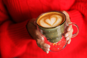 Young woman holding a cup with Christmas motifs of green and gold stars, she has prepared a specialty coffee.