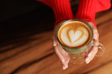 Hands of a woman in a red sweater holding a Christmas cup of coffee. Latte art, caffeine to start the day with energy. Customer, student or businesswoman having breakfast in store or cafe.