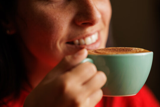 Portrait of a beautiful smiling lady enjoying the aroma of specialty coffee and drinking cappuccino from a cup while resting in the restaurant. Portrait, close up.