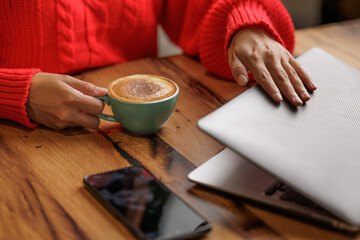A young woman enjoys a coffee break, sitting at the work table with her computer and mobile phone. Close-up of hands closing the laptop at the end of work.
