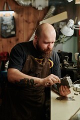 Bearded worker of plastic recycling workshop using caliper while checking dimensions of new metal detail or mold cast