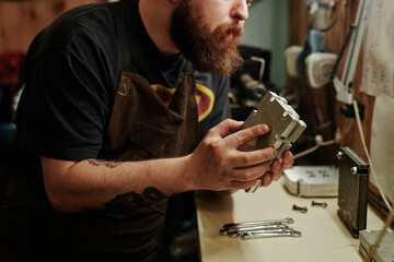 Bearded technician or engineer of recycling factory putting together two parts of metallic press mold by workbench