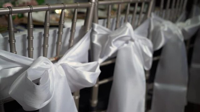 Stylishly crafted white satin bows tied onto exquisite silver chiavari chairs, creating a perfect aesthetic for weddings and elegant events that call for a touch of sophistication and beauty