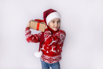 A cheerful child in festive attire holds a Christmas gift while smiling against a white background during the holiday season