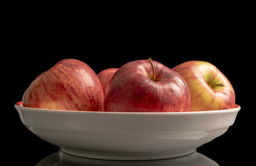 Several red apples in a ceramic dish, macro, isolated on a black background.