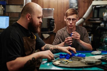 Two young factory technicians sitting by workplace in plastic recycling workshop and sorting supplies before processing