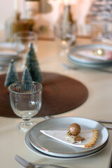 Table set for Christmas meal with plates, glasses, holiday decorations, lit candles and wine. Selective focus.