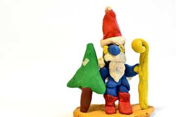 Santa Claus holds a green Christmas tree in one hand and a staff in the other and stands on a stand.