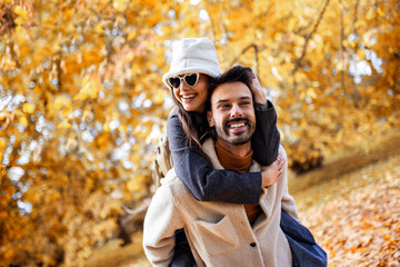 Boyfriend giving girlfriend piggy back ride in a colorful park on a sunny autumn day.