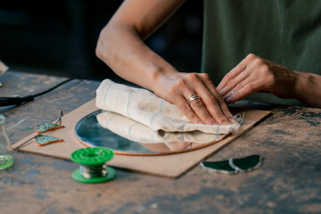 close up in a large green workshop, a woman with green hair creates decorative flowers laying them out on a round mirror, handmade with a soldering iron.