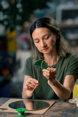 in a large green workshop, a woman with green hair creates decorative flowers laying them out on a round mirror, handmade with a soldering iron.