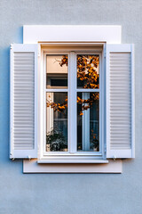 Fototapeta premium A serene view of a white window with wooden shutters reflecting autumn leaves in a peaceful neighborhood setting